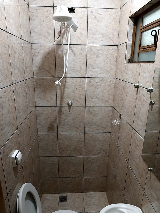 Banheiro do Hotel Costa com box de vidro, chuveiro e vaso sanitário