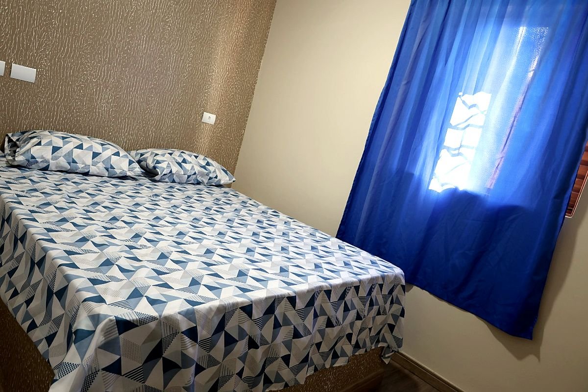 Quarto de casal do Hotel Costa com cama arrumada e cortina azul na janela