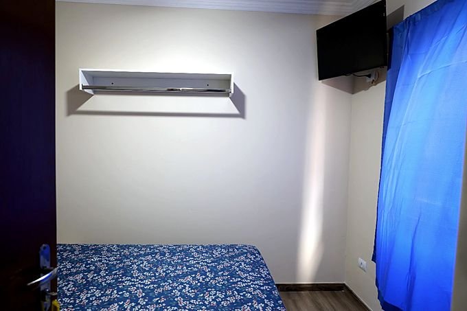 Quarto do Hotel Costa com televisão na parede e prateleira de apoio