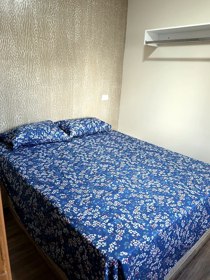 Quarto de casal do Hotel Costa com colcha azul e prateleira na parede