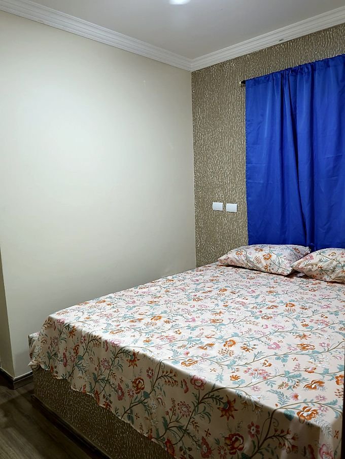 Quarto do Hotel Costa com cortina azul, luminária de teto e cama de casal
