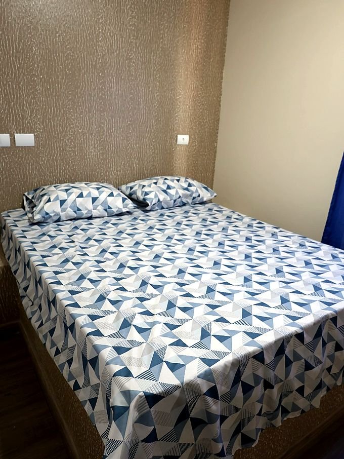 Quarto de casal do Hotel Costa com colcha geométrica e cabeceira de papel de parede
