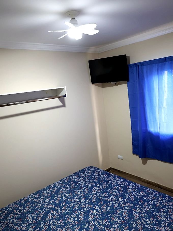 Quarto do Hotel Costa com televisão, prateleira de apoio e cortina azul