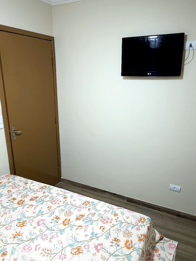 Quarto do Hotel Costa com televisão na parede, porta de madeira e cama de casal