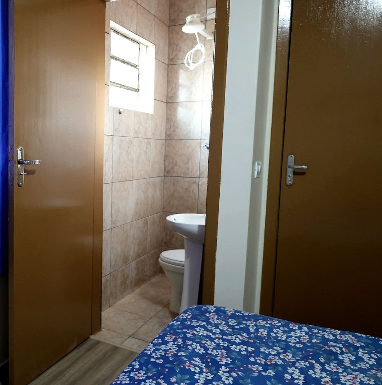 Suíte do Hotel Costa com a porta do banheiro privativo aberta, mostrando pia, vaso e chuveiro